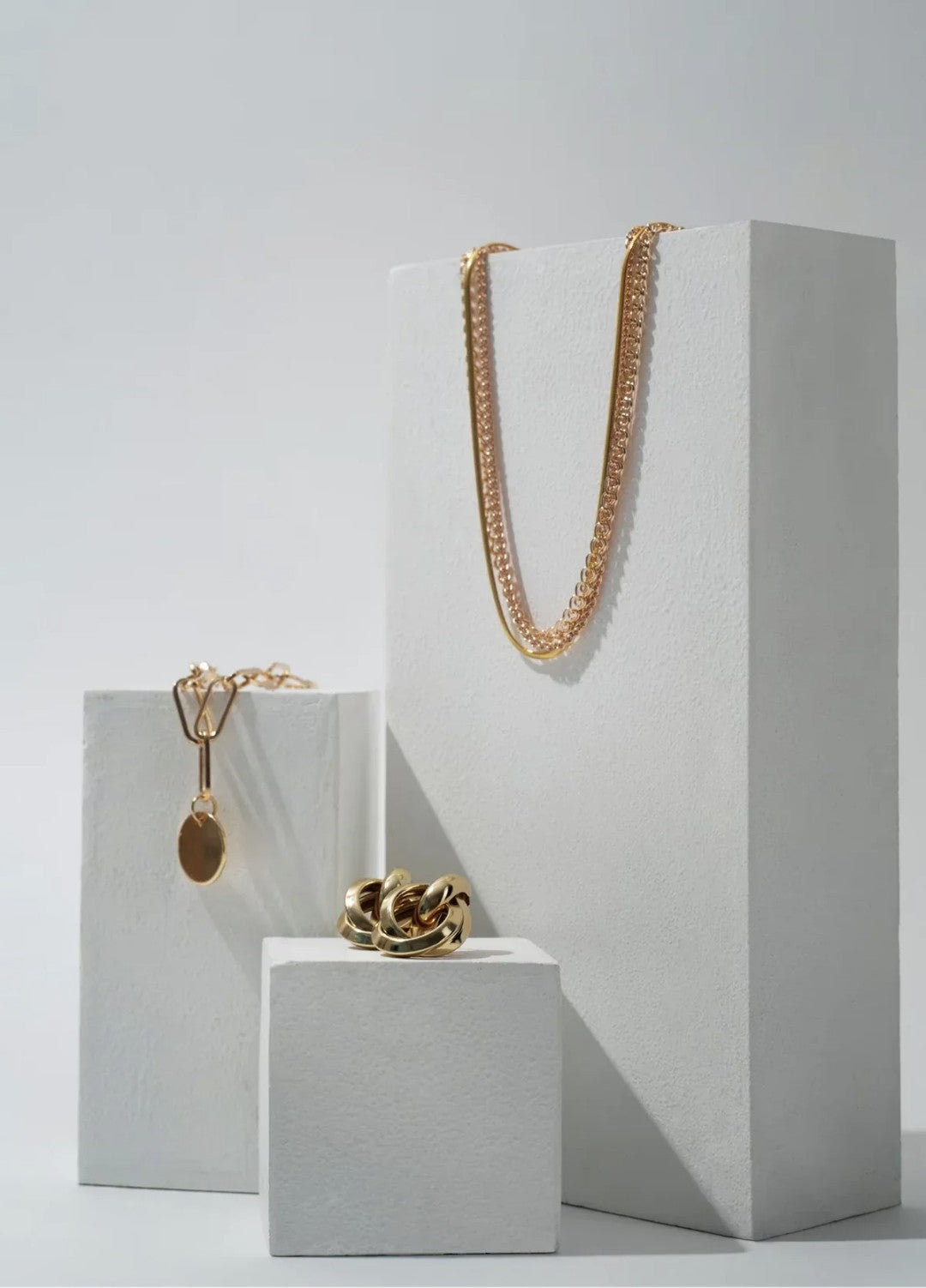 Gold chain necklace, hoop earrings, and pendant on white blocks
